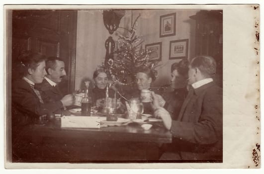 GERMANY - CIRCA 1940s: Vintage photo shows family sits at the table during Christmas time. In the room is a Christmas tree.