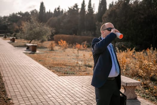 Mature entrepreneur drink coffee in autumn park. Senior executive rest in city park.