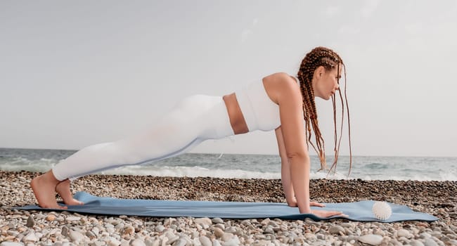 Woman yoga sea. Well looking middle aged woman with braids dreadlocks in white leggings and tops doing stretching pilates on yoga mat near sea. Female fitness yoga routine concept. Healthy lifestyle
