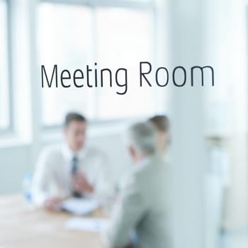 Behind closed doors. Closeup of a glass door reading meeting room with business people blurred in the room behind