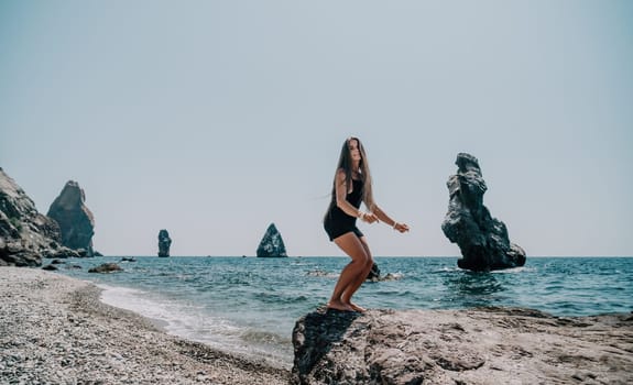 Woman travel sea. Young Happy woman in a long red dress posing on a beach near the sea on background of volcanic rocks, like in Iceland, sharing travel adventure journey