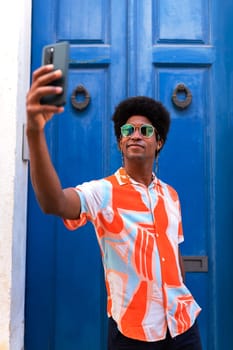 Vertical portrait of young African American man taking selfie with mobile phone outdoors. Lifestyle concept.