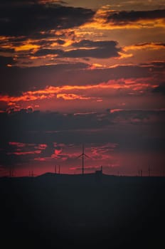 Scenic vertical view of an agricultural field with windmills during a mesmerizing sunset