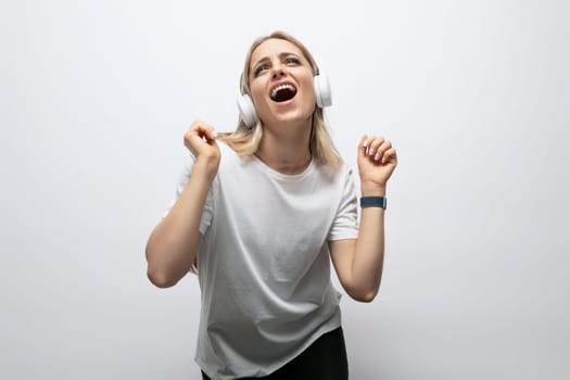 a girl in a white t-shirt listens to music in wireless headphones on a white background with empty space.