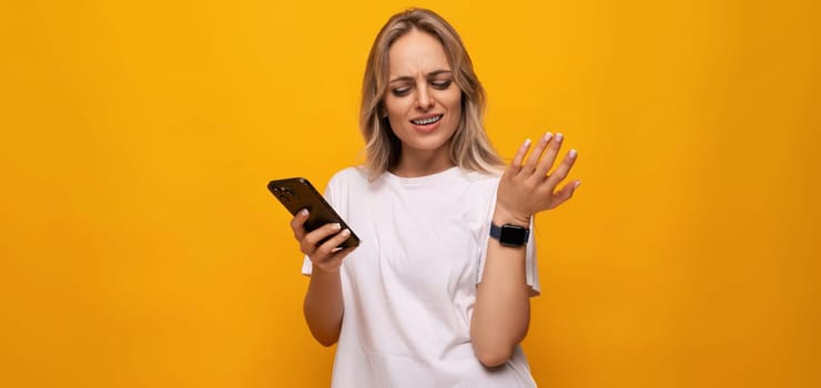 a woman in a white T-shirt with a smartphone in her hands uses an application on a yellow background.