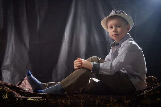 Stylish and fashionable young boy in shirt and hat in the studio on a black fabric background with flashes. Contour portrait of a male model