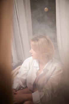 Portrait of sexual body positive adult lady woman in intimate in tender space indoors in a bedroom. Plump girl poses in black underwear and white shirt during boudoir style photo shoot