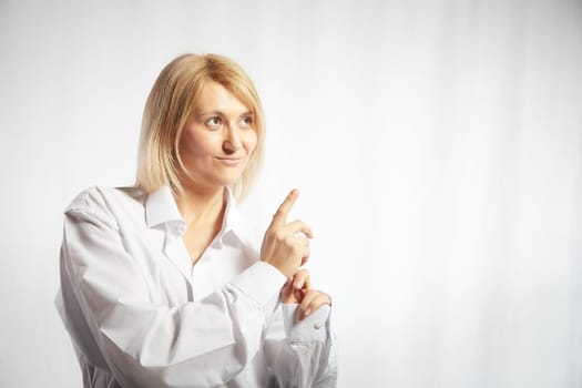 Portrait of a pretty blonde smiling woman posing on white background and pointing somewhere. Happy girl model in white shirt posing in studio. Copy space