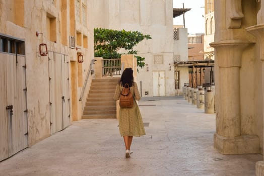 A woman with a backpack walks through the streets of the old city of the Emirates in the Persian Gulf. Mud houses of Al-Sif. Deira, Burdubai. Travel and sightseeing concept.