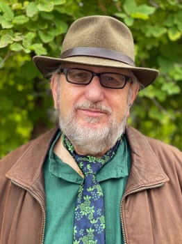 Elderly man with beard, glasses and hat looking into the camera. He wears his tie direct on his neck over his shirt. He's an individualist.