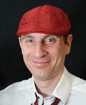 Portrait of a man with a  red flat cap looking into the camera. Dark grey background.