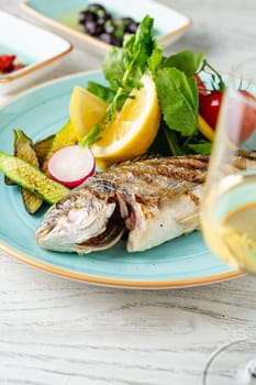 Grilled sea bream with vegetables and greens on wooden table