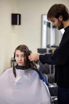 male hairdresser is combing the hair of the female client. hairdresser doing hair to his client woman