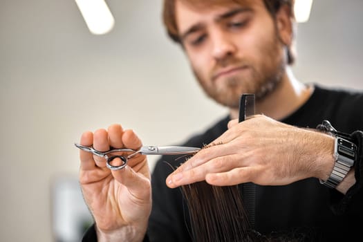 Professional male hairdresser with scissors cutting female hair in salon