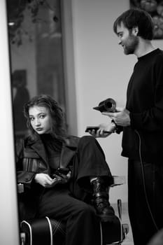 man hairdresser using hair dryer for female hair after washing in the beauty salon.