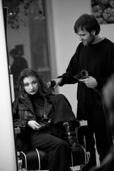 man hairdresser using hair dryer for female hair after washing in the beauty salon.