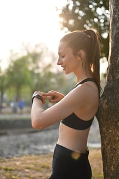 Portrait of sport caucasian woman in sportswear looking smart watch checking result jogging in city park outdoor.