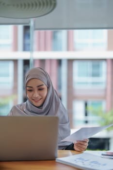 A beautiful Muslim woman showing a smiling face in the morning using computers and documents working at the office.