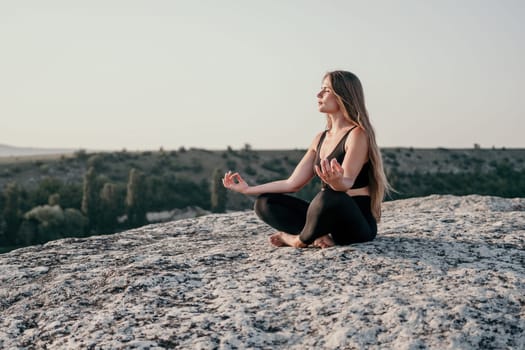 Well looking middle aged woman with long hair, fitness instructor in leggings and tops doing stretching and pilates on the rock near forest. Female fitness yoga routine concept. Healthy lifestyle.