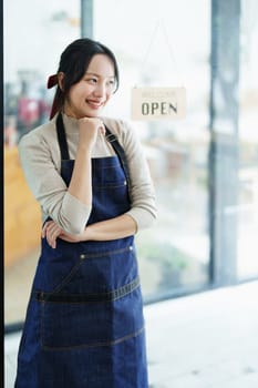 Starting and opening a small business, a young Asian woman showing a smiling face in an apron standing in front of a coffee shop bar counter. Business Owner, Restaurant, Barista, Cafe, Online SME.