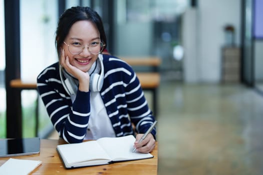 Portrait of a beautiful young Asian student using a notebook to take notes in the library.