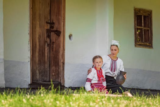 mother and daughter in traditional Ukrainian clothes are sitting near the house