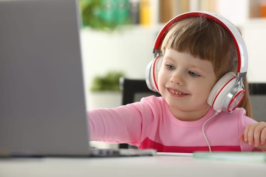 Portrait of a little child girl in headphones with laptop. Watching cartoons and kids remote learning concept