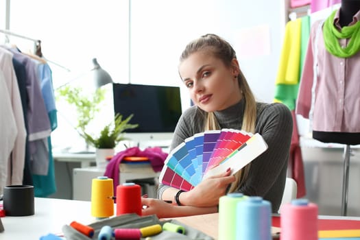 Female fashion designer seamstress working in studio holding color palette. Selection and choice of color solution in concept clothing collection