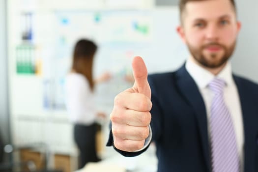 Businessman showing thumb up sign of success over blurred team of business people. Business consultant recommendation and successful career