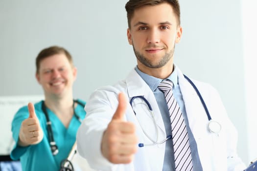 Two doctors gesture thumbs up in clinic recommending medical services. Health insurance and quality services concept