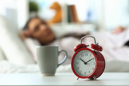 Red alarm clock at ten o'clock and sleeping woman. Peaceful sleep and late rise concept