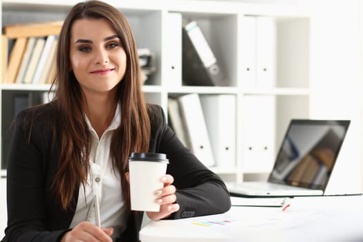 Beautiful young businesswoman holding glass of coffee at workplace. Break and rest in office concept