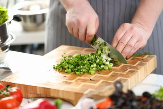 Closeup of hands of cook holding knife for cutting green onions. Sliced fresh green onions and cooking vegetables in kitchen