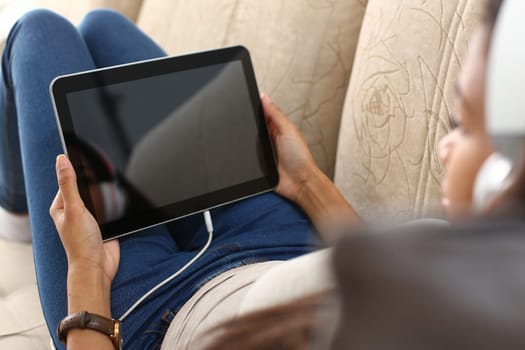Woman in headphones holds tablet and lies on sofa. Applications for watching movies or learning concept
