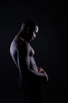 Athletic african american man topless, big muscles, a dark background studio