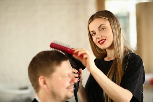 Woman in hairdresser hairdresser makes ahairstyle with hair dryer for male client. Stylish trendy hairstyle concept