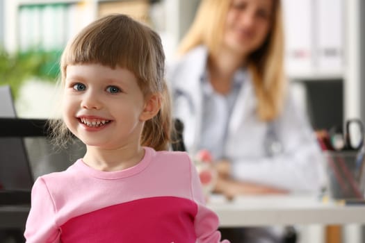 Portrait of little smiling baby girl in background sits doctor. Children health insurance and pediatrician services