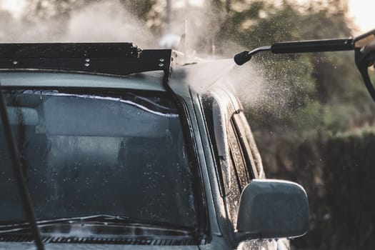 Close-up of washing car with high-pressure water hose on car wash service, splashing water around.