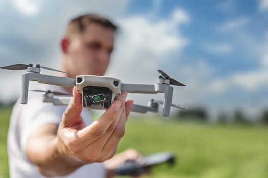 A quadcopter operator with a remote control out of focus holds a drone in front of him in focus outdoor.