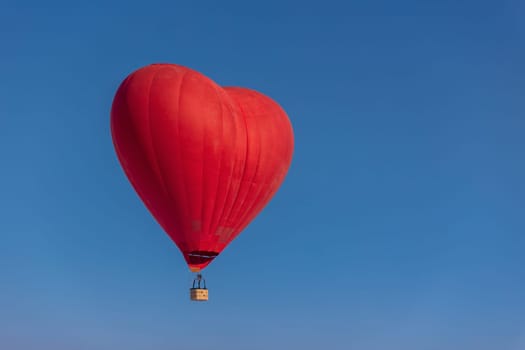 Hot air balloon in the shape of a heart in the blue sky. Honeymoon concept for newlyweds.