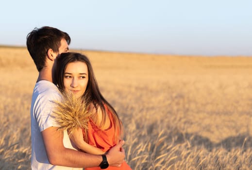 Young man hugging his girlfriend on sunset in wheat field. Copy space, love, togetherness concept