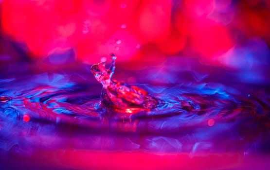 A transparent drop with a red-violet background falls into the water. Abstract colorful background