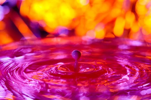 A drop falls into a dense liquid with a red background. Abstract colorful background