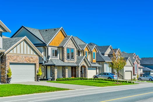 A perfect neighborhood. A street of family houses in suburban area of Vancouver with concrete side walk and asphalt road in front. Residential houses with cars parked on driveways.