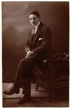 BARMBEK, GERMANY - CIRCA 1930s: Vintage photo shows young man wears suit and sits on the sofa. Photography with sepia effect.