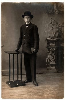 THE CZECHOSLOVAK RAPUBLIC - CIRCA 1920s: Vintage photo shows an elegant boy wears black suit, black gloves and bowler hat. Boy holds a small pocketbook (billfold). Black white antique photography.