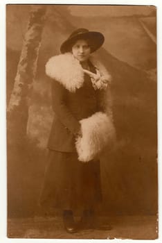 GERMANY - CIRCA 1920s: Vintage photo shows woman wears white fur corral and white muff. An elegant woman wears wide-brimmed hat.