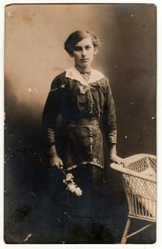 GERMANY - CIRCA 1930s: Vintage photo shows young woman poses next to historic wicker armchair. Black white antique studio photography.