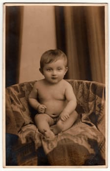 PLZEN (PILSEN) - FEBRUARY 24, 1932: Vintage photo shows small baby sits on an armchair. Black & white antique photography with sepia effect.