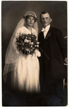 CHRASTAVA KRATZAU , THE CZECHOSLOVAK REPUBLIC - CIRCA 1930s: Vintage photo of newlyweds. Bride wears a long veil and holds wedding bouquet. Groom wears black suit and white bow tie. Black white antique studio portrait.